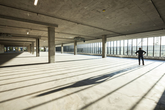 Single businessman exploring new empty raw business space for a new office, light streaming in large windows. 