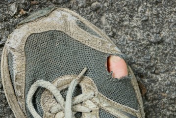 gray old ragged sneaker with a finger on the asphalt