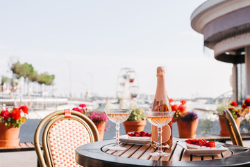 close-up view of two glasses of champagne, champagne bottle and sweet desserts on round table in outdoor cafe