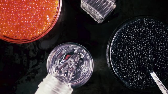 Slow motion black and red caviar and pour ice vodka in a glass top view