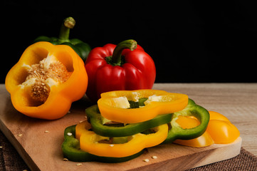 Colourful green,yellow and red peppers are slice placed on a wooden tray ready for cooking with black background,Selective focus