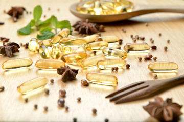 Medicine herb, Cod liver oil omega 3 gel capsules spread on top of woodwn desk with healthy medicinal plant, spoon and fork.