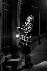 Fototapeta na wymiar Beautiful blonde woman detective in stylish retro coat holding old lantern, french noire atmosphere concept