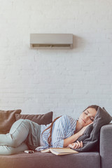 woman sleeping on sofa with book and air conditioner on wall