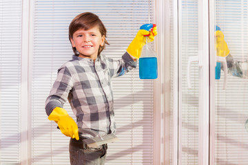 Cute boy washing windows in yellow rubber gloves