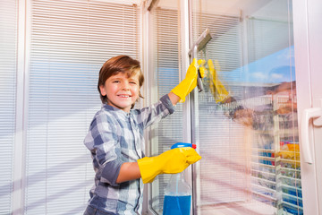 Smiling boy washing windows with window cleaner