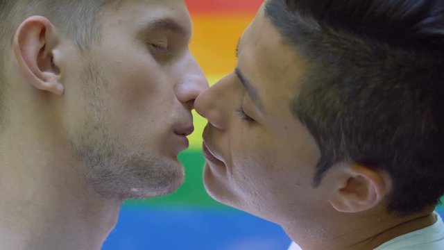 Young men kissing close-up on rainbow flag behind, gays rights acceptance, love