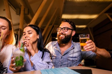Cheerful friends drink beer with cocktails at the bar
