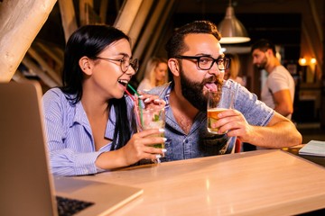 Friends watch the match on a laptop in a bar with glasses of Mojito
