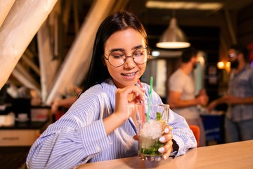 Girl in glasses with Mojito in hand is behind the bar