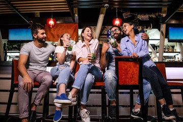 Five cheerful friends sit at the bar in the night club talking and laughing with each other