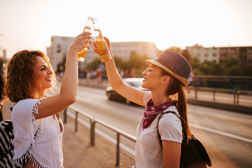Two beautiful hipster girls toasting in the city street in the summer.