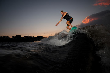Wakesurfer jumping on board riding down the river waves at the sunset