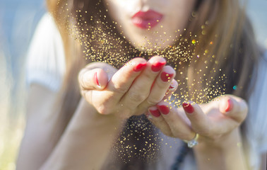 Young woman blowing magic gold dust from her hand