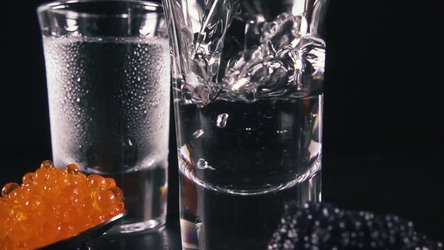 Slow motion frozen glass of vodka near black and red caviar and pour vodka into the glass
