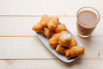Top view and close up: Deep-fried dough stick on a white plate with a glass of hot coffee (Thai breakfast style) on wooden background.  