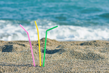 Fototapeta na wymiar Plastic colored straw tubules for drinking in the sand on the beach. Concept