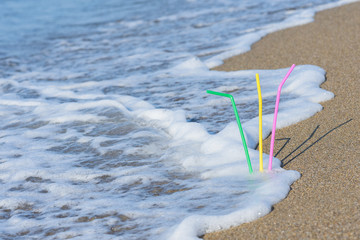 Fototapeta na wymiar Plastic colored straw tubules for drinking in the sand on the beach. Concept