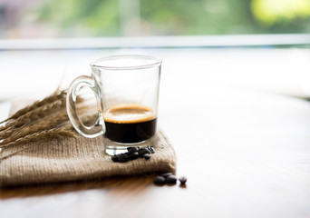 Black coffee in glass with coffee beans, on wood table