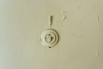 Old plastic light switch on a common walled wall covered with a thick layer of oil paint inside a fresh room