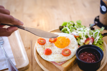 eating knife preparing to hit fried egg on Sandwich ham cheese serve with wooden plate