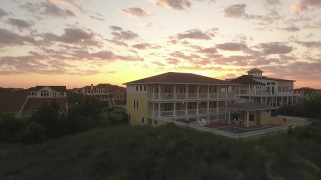 This is a shot of a drone flying over a house on the beachfront of the Outer Banks in North Carolina to reveal dozens of houses on the island during sunset.