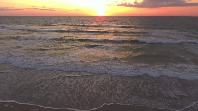 This is a video of a drone flying along the beach looking out at the waves and the ocean during sunrise.