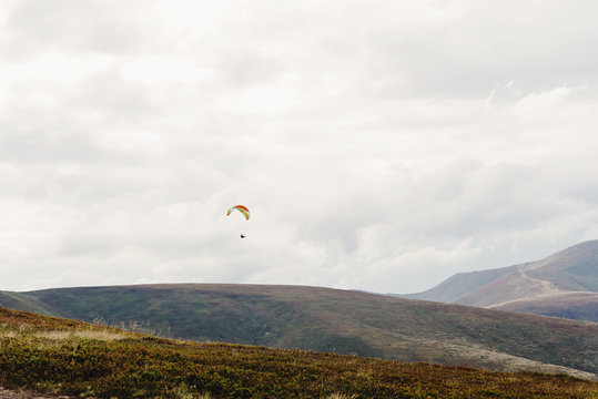 parachute skydiver flying in clouds at mountains, travel adventure concept, space for text