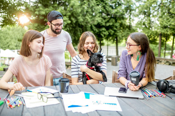 Friends having fun together sitting with dog during a study outdoors at the park cafe