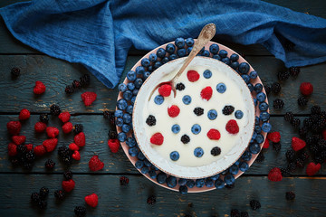 white yoghurt with frefh blueberries and raspberries in the white bowl on the dark wooden table