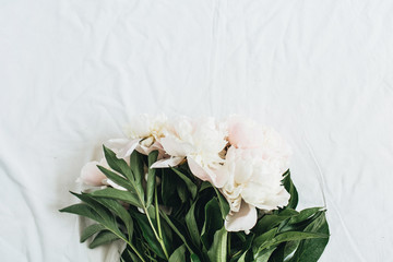 Flat lay, top view of white peonies flower bouquet on white blanket background.