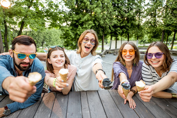 Obraz premium Young friends having fun with ice cream sitting together outdoors in the park