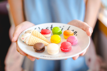 Mix color of macaroon on wihte plate with french language holding on girl hand in blue
