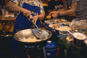 Woman cooking put onion slice into pan with people are eating in background