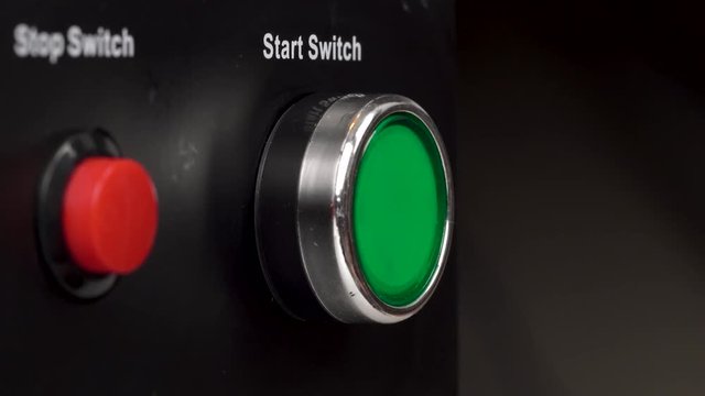 Closeup of two buttons in the frame. Green start switch and red stop switch buttons. Finger press the green start switch button.