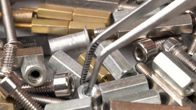 Heap of pcb stand spacers, screws and nuts. Choosing the right one using the tweezers. Closeup macro.