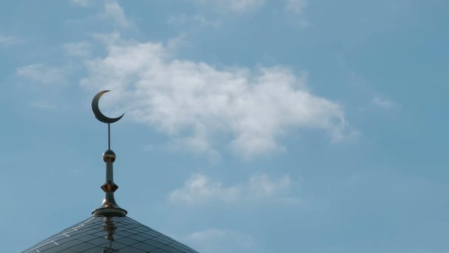 The clouds float past the golden crescent on the top of the mosque minaret. A symbol of the Muslim religion. A sunny day with a blue sky.