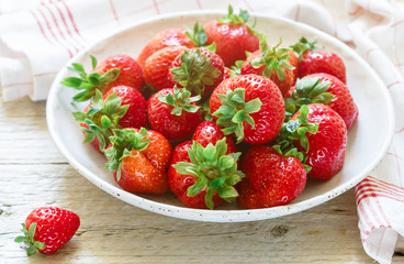 Fresh ripe organic strawberries in a white plate on a wooden table. Summer berry. Rustic style