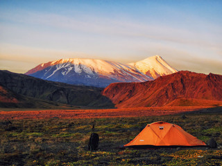 Tent and tourist backpack behind Tolbachik volcano on sunset time