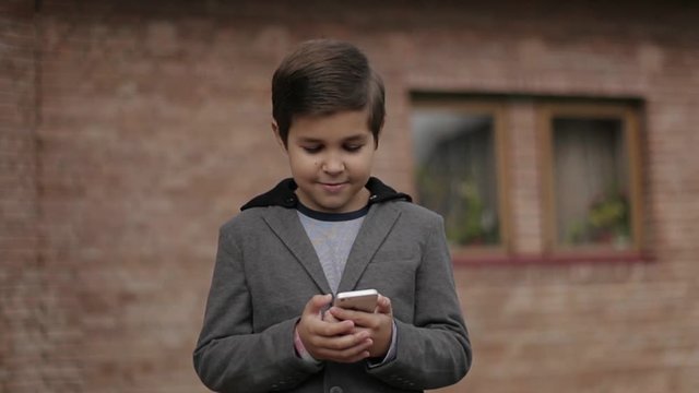 Handsome little Boy use his phone. Background of bick wall