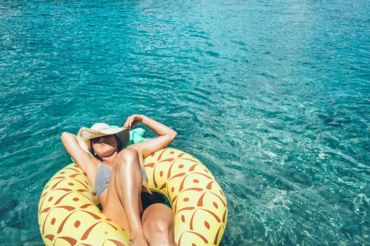 Woman swims on inflatable pineapple pool ring in crystal clear sea lagoon
