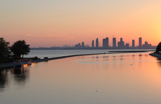 Sun setting on Lake Ontario looking at a skyline of condos in Etobicoke from the shore in Toronto while a kayaker paddled in the far distance