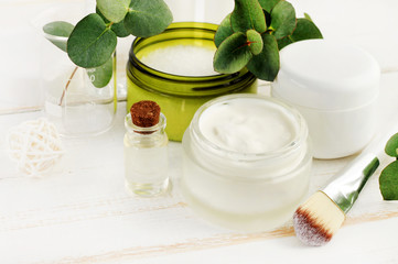 Obraz na płótnie Canvas Making herbal beauty care remedy of oil, green holistic plants, fresh cream, sea salt. Jars and bottles with cosmetic products set on white wooden table. 