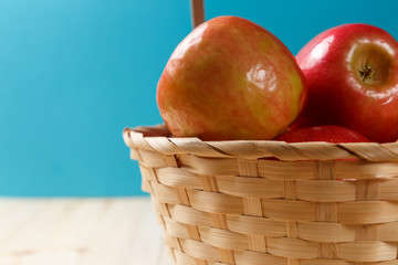 Ripe red apples in a basket on a bright wooden background