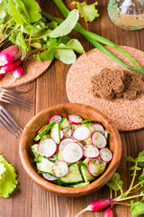 Lenten spring vegetable salad of cucumber, radish, greens and sunflower oil in a plate on a wooden table