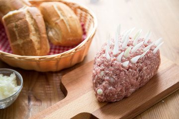 Mettigel aus Schweine Mett und Zwiebeln auf Holzbrett mit Brotkorb für Party