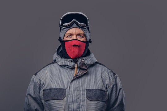Portrait of a snowboarder dressed in a full protective gear for extream snowboarding posing at a studio. Isolated on a gray background.