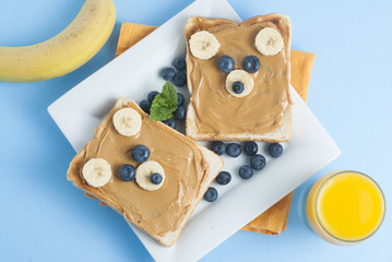 Fototapeta na wymiar Breakfast Toast Bear Shaped Peanut Butter Banana Bread Blueberry for Kids. Funny animal face toast for kids snack. Blue Background.