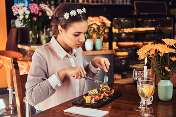 Portrait of a beautiful black-skinned woman wearing a blouse and flower headband, enjoying dinner while eating in a restaurant.