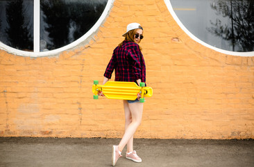 Young cheerful girl posing with yellow skateboard against orange wall